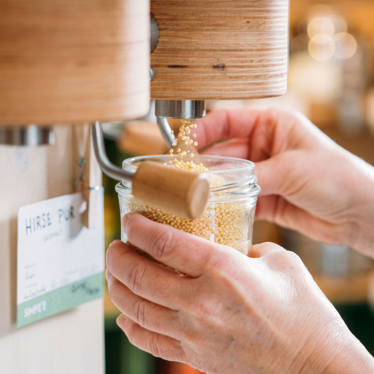 Abfüllstation. Zwei Hände füllen Hirse in ein Glas